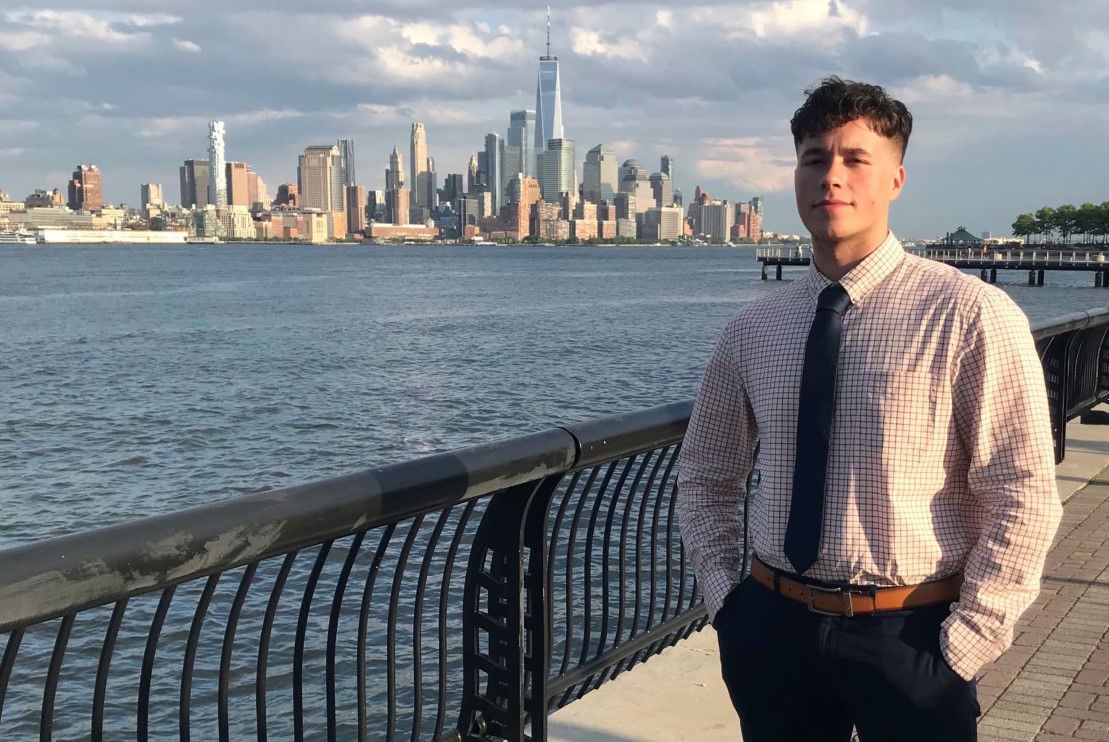 Lucas Bastos across the Hudson River standing in front of the New York skyline